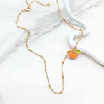 Gold necklace with a madarin-shaped pendant on a marble surface