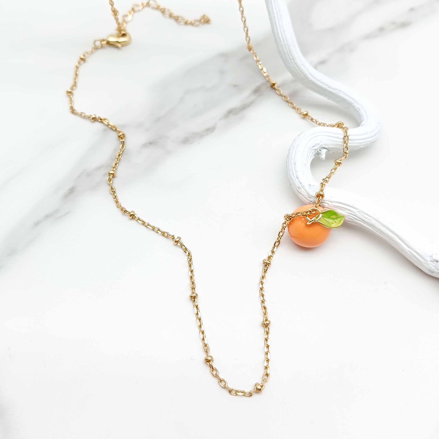 Gold necklace with a madarin-shaped pendant on a marble surface