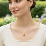 Woman wearing a gold necklace with an orange pendant outdoors