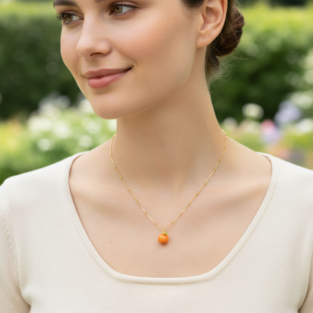 Woman wearing a gold necklace with an orange pendant outdoors
