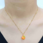 Gold necklace with a small orange pendant on a mannequin