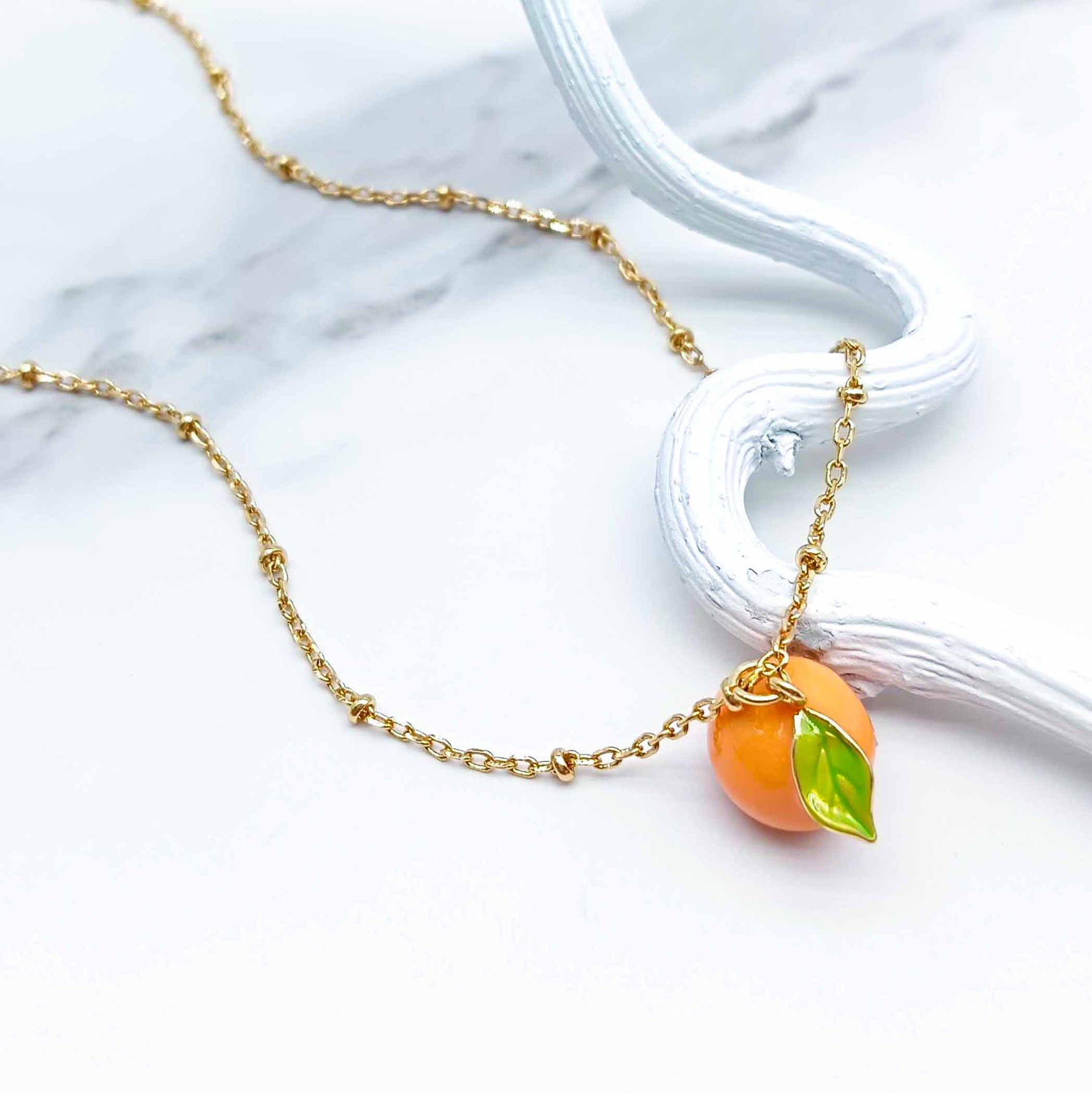 Necklace with orange-shaped pendant on a marble surface