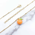 Gold chain necklace with an orange fruit charm on a marble background