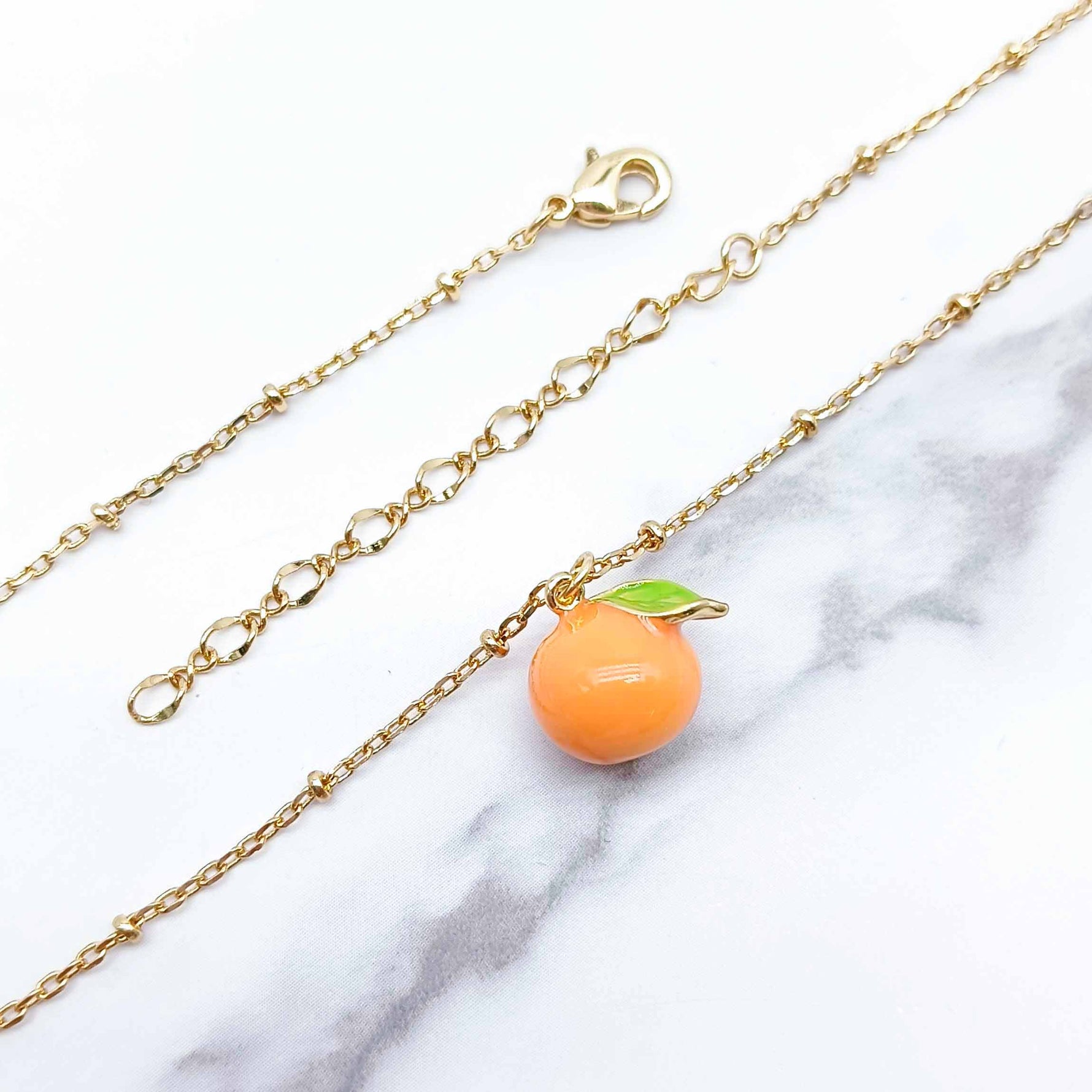 Gold chain necklace with an orange fruit charm on a marble background