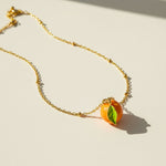 Gold necklace with a mandarin-shaped pendant on a light background
