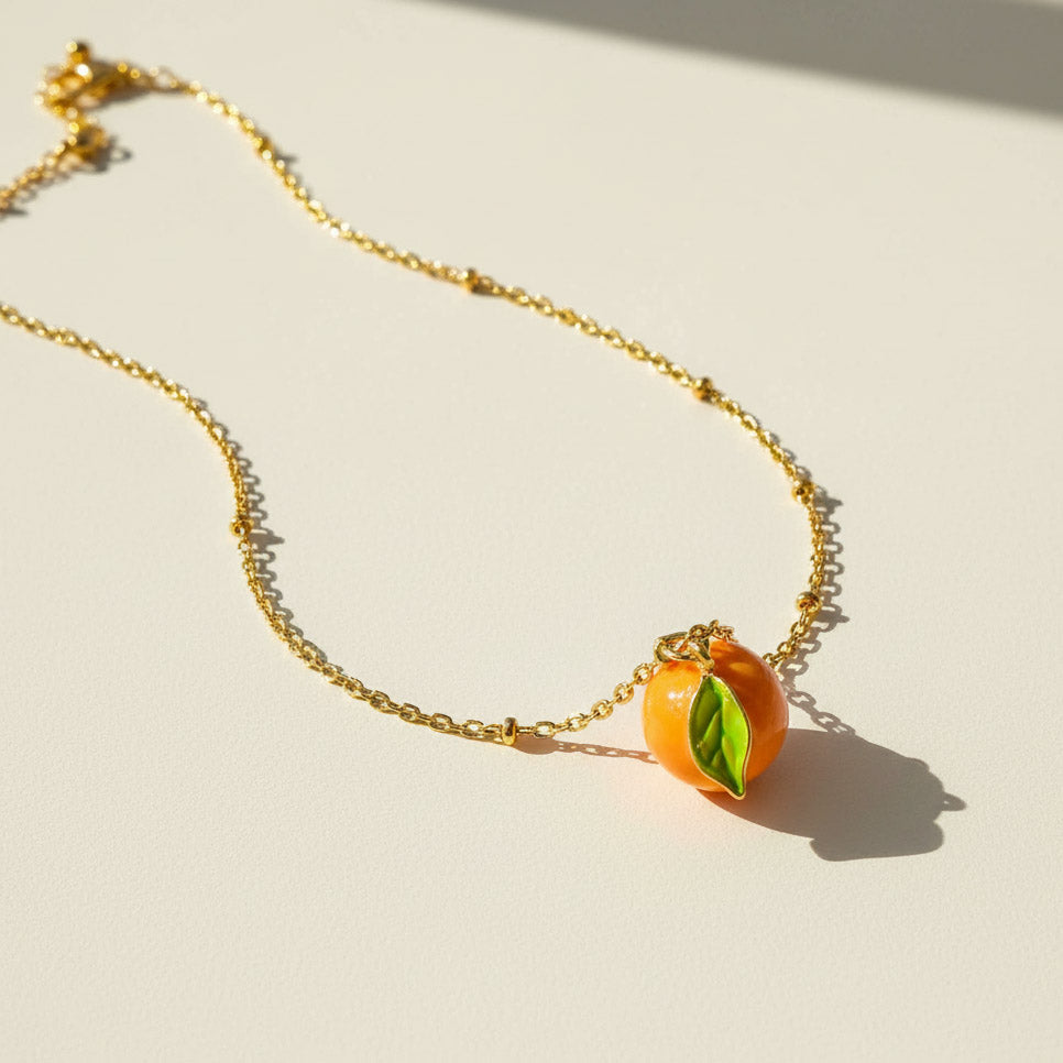 Gold necklace with a mandarin-shaped pendant on a light background