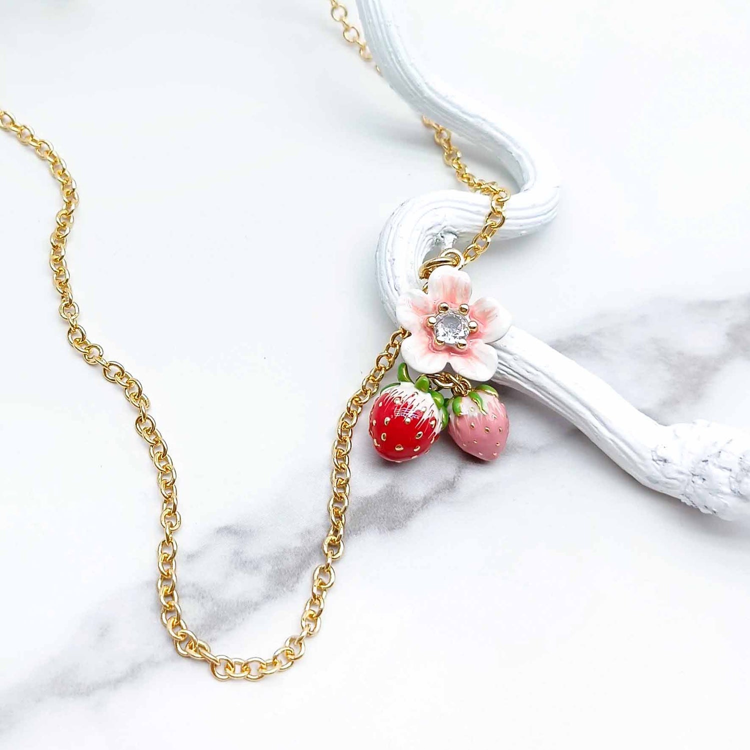 Necklace with strawberry and flower pendant on a marble surface