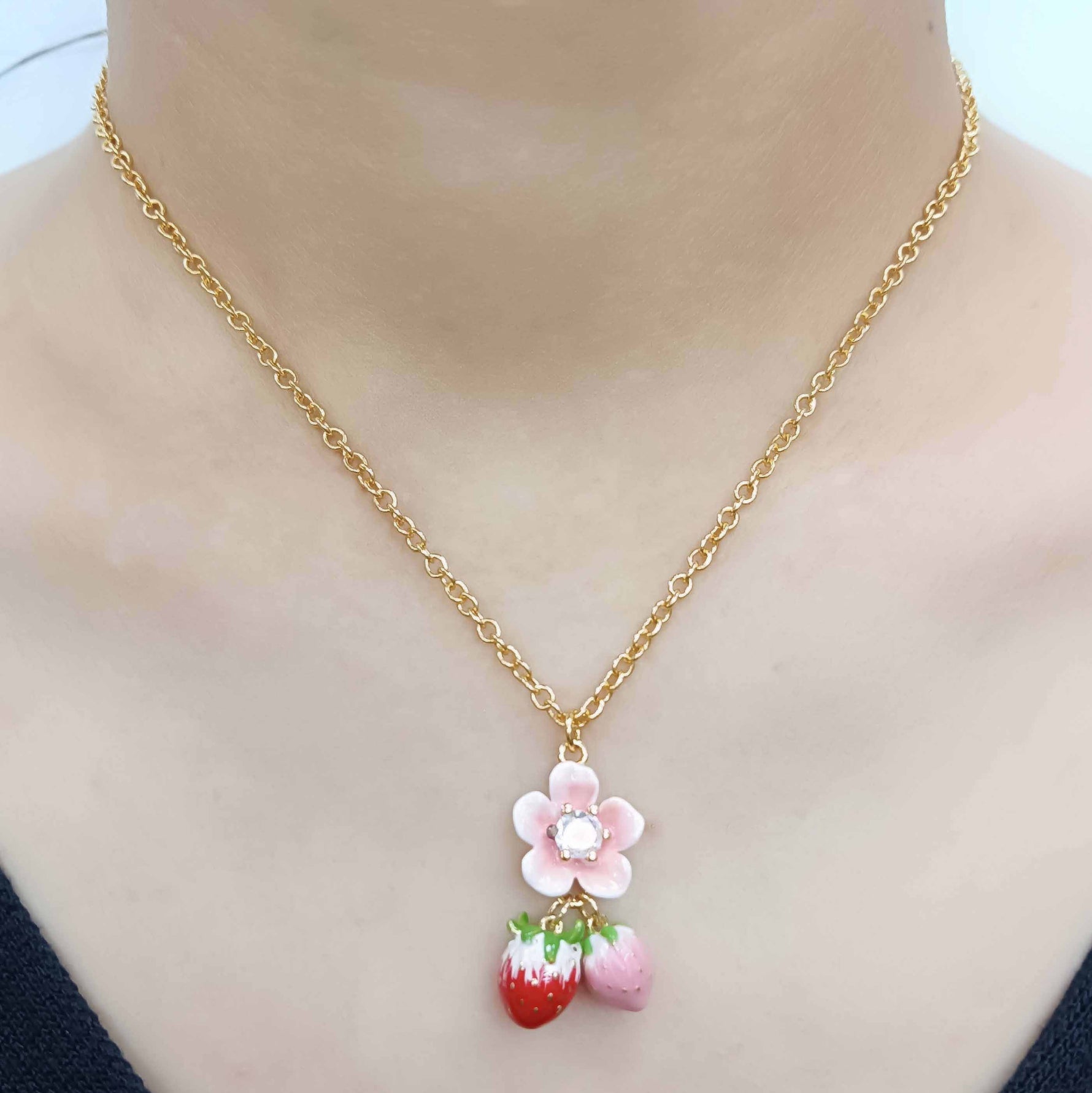 Gold necklace with a pink flower and red strawberry pendant on a mannequin.