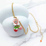 Necklace with floral and strawberry pendant on a white surface
