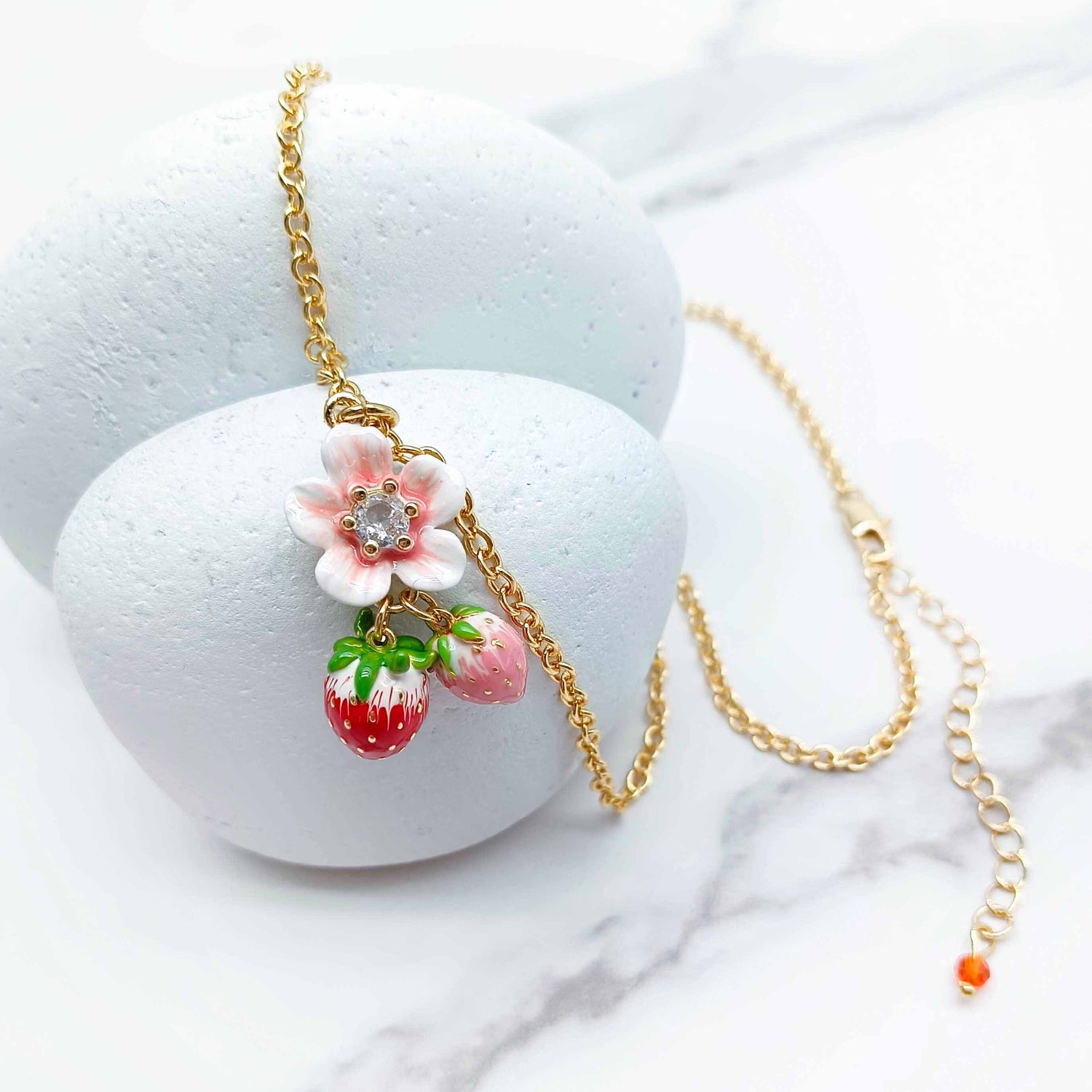 Necklace with floral and strawberry pendant on a white surface