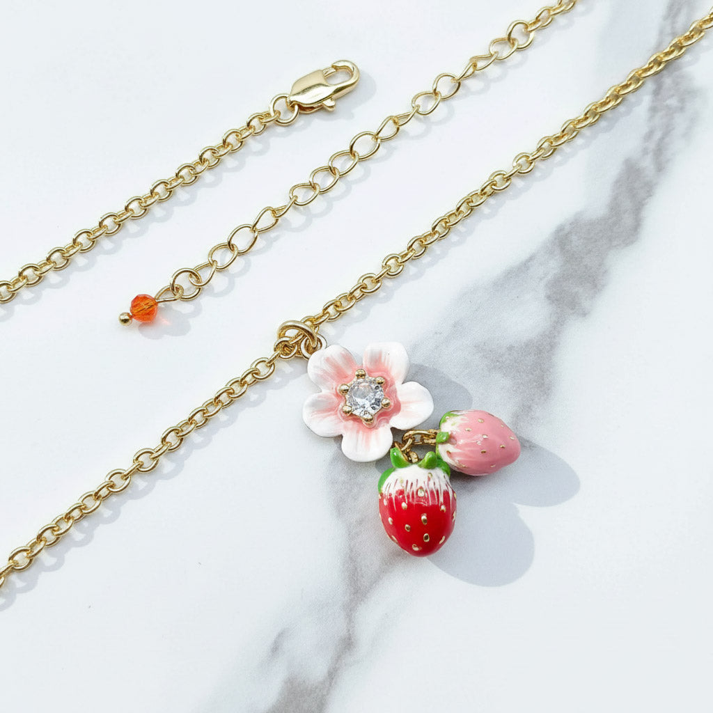 Gold chain bracelet with strawberry and flower charm on a marble surface