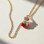 Necklace with strawberry and flower pendant on a light background