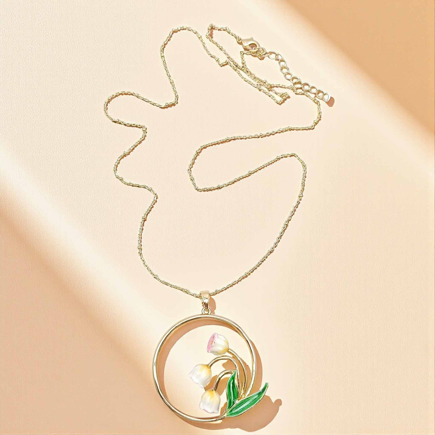 Gold necklace with a floral pendant on a beige background