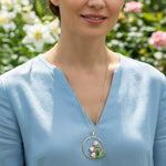 Woman wearing a gold necklace with a floral pendant against a blurred floral background
