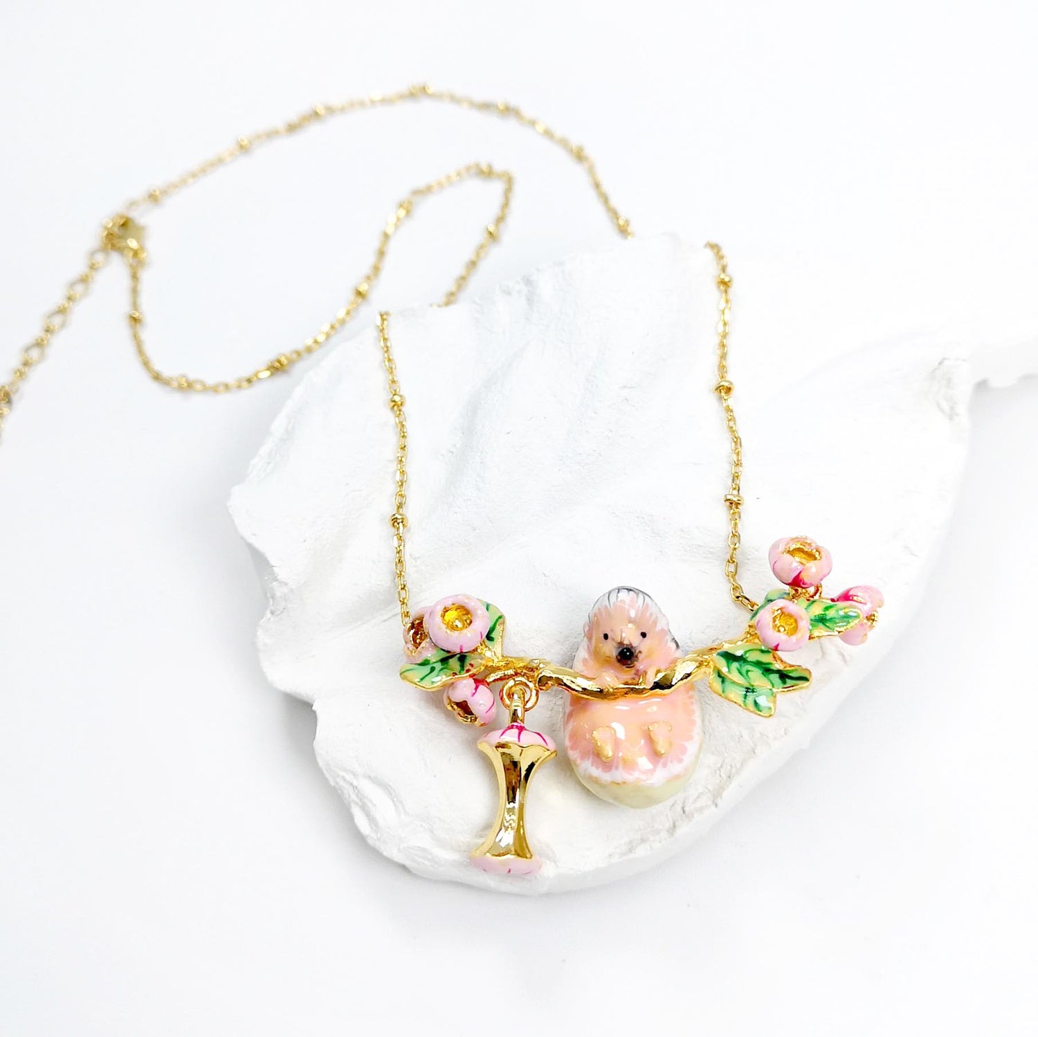 Necklace with a hedgehog and flower pendant on a white dish