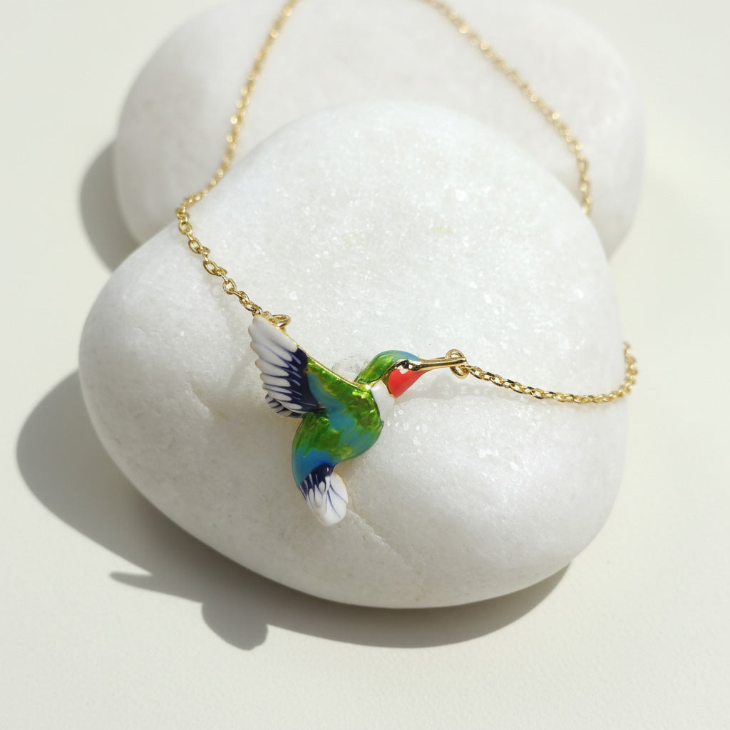Colorful bird-shaped pendant on a gold chain against a white stone background