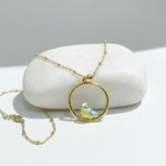 Gold necklace with a bird pendant on a white stone surface