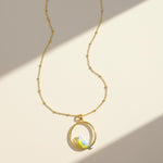 Gold necklace with a round pendant featuring a bird design on a beige background