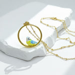 Gold necklace with a bird pendant on a white stone surface