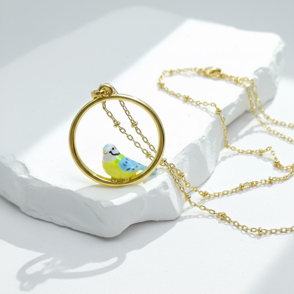 Gold necklace with a bird pendant on a white stone surface