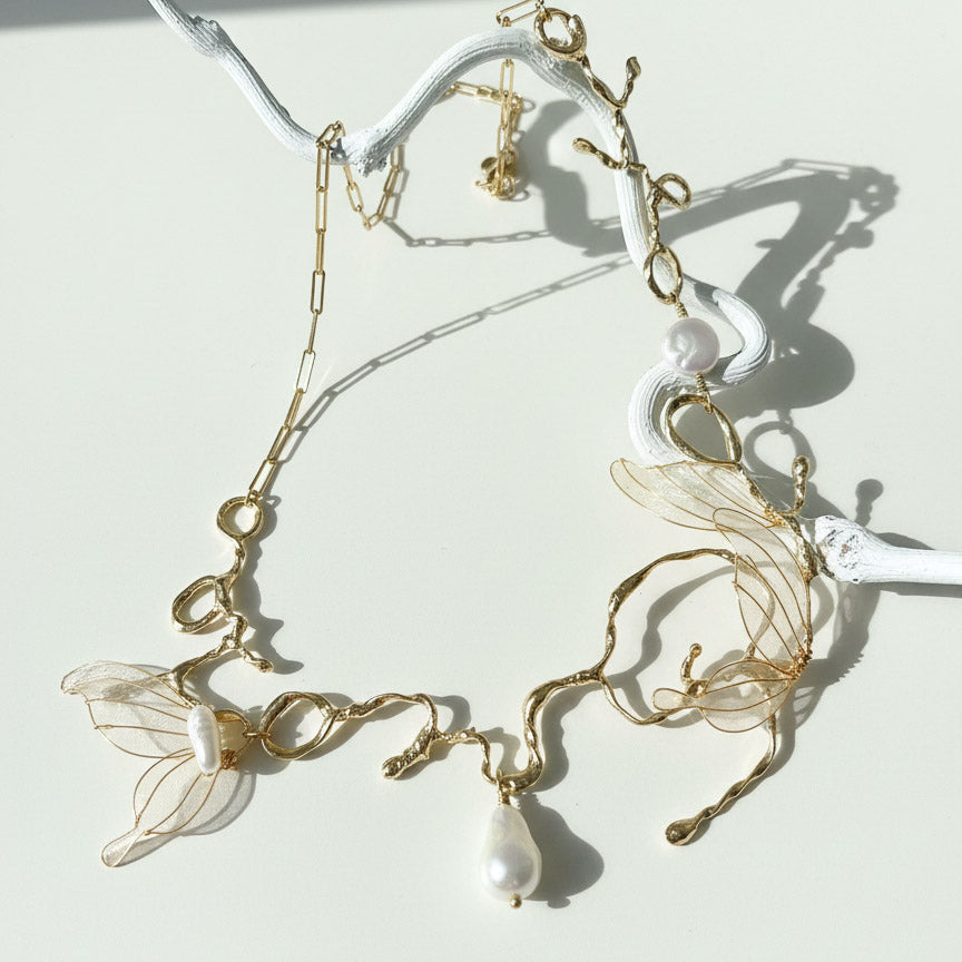Delicate gold necklace with leaf designs and pearls on a white background
