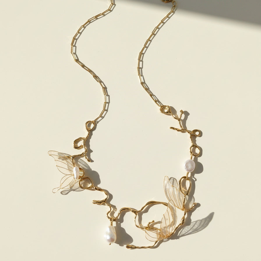 Gold necklace with butterfly and pearl details on a beige background