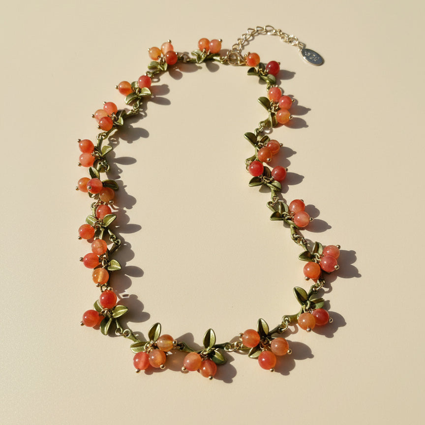 Necklace with orange beads and green leaves on a beige background