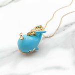Blue whale-shaped pendant on a gold chain against a marble background
