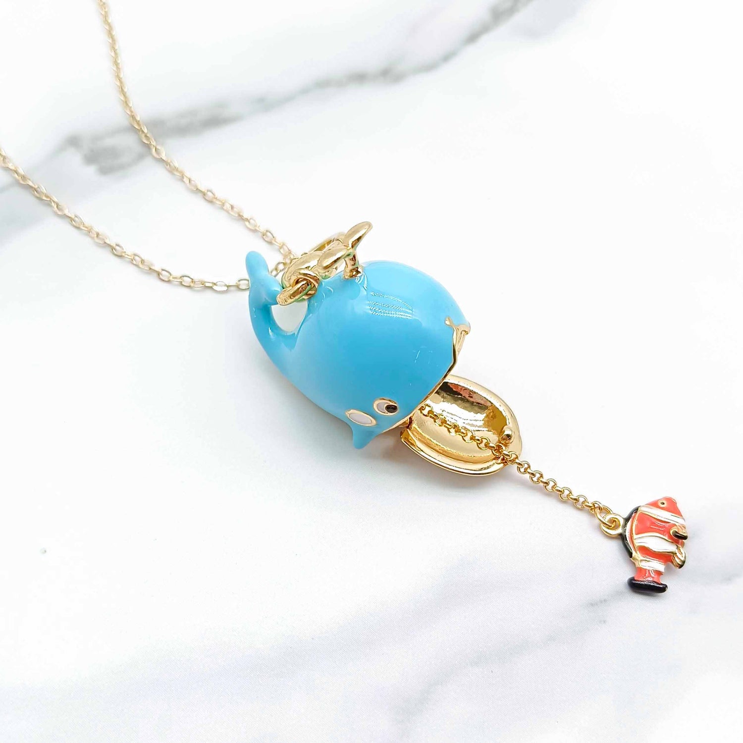Necklace with a blue whale pendant and a small fish charm on a marble surface