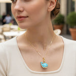 Woman wearing a gold necklace with a blue whale pendant outdoors.