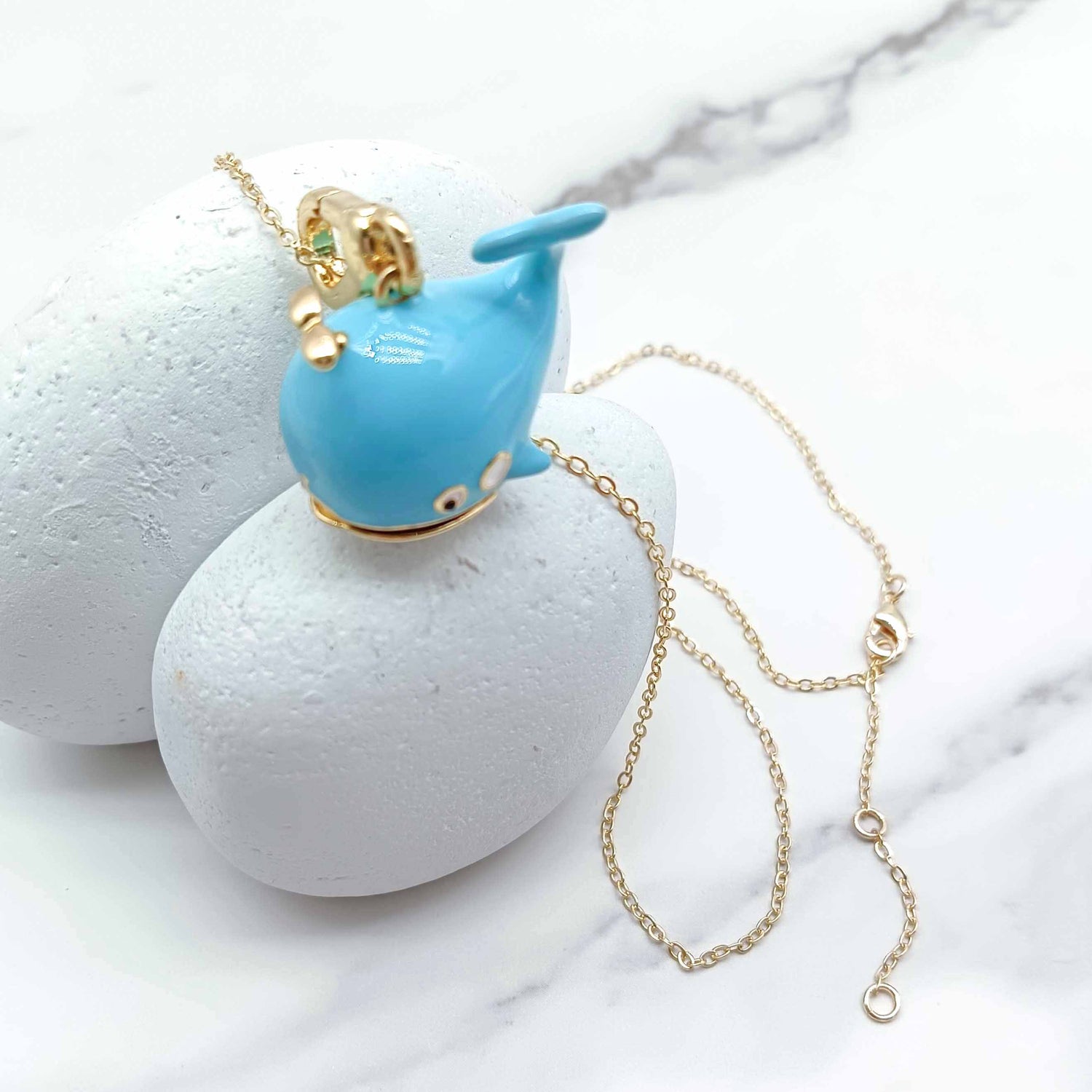 Blue whale-shaped pendant on a gold chain against a marble background