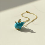 Turquoise whale pendant on a gold chain against a light background