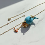 Necklace with a blue whale pendant and orange fish charm on a light background