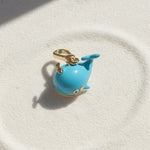 Blue whale-shaped charm on a gold chain against a white background