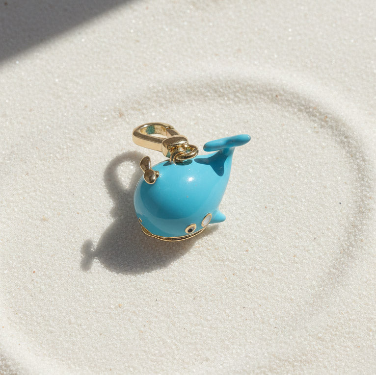 Blue whale-shaped charm on a gold chain against a white background