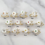 Adjustable gold-plated birthstone rings for each month, featuring hand-carved mother-of-pearl flowers and cubic zirconia accents, displayed on a marble background.