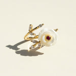 Gold ring with a white flower and red gemstone on a beige background