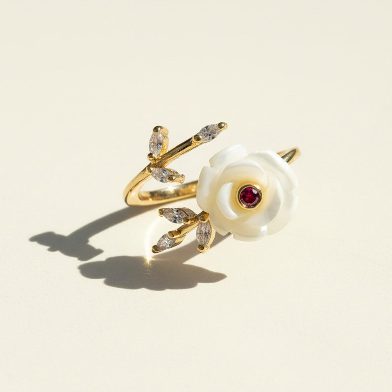 Gold ring with a white flower and red gemstone on a beige background