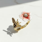 Gold ring with a pink floral design and bee on a white surface
