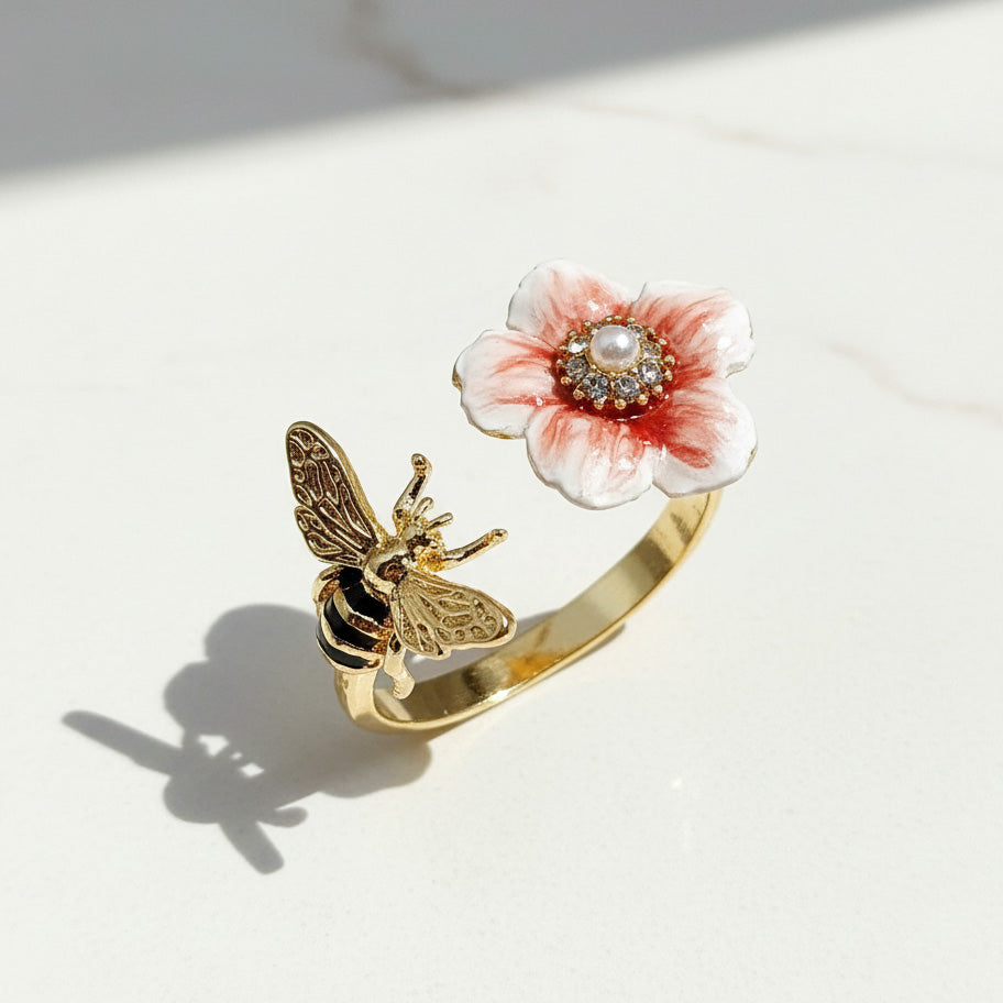 Gold ring with a pink floral design and bee on a white surface
