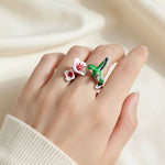 Hand wearing a ring with a green bird and red flower design on a beige background