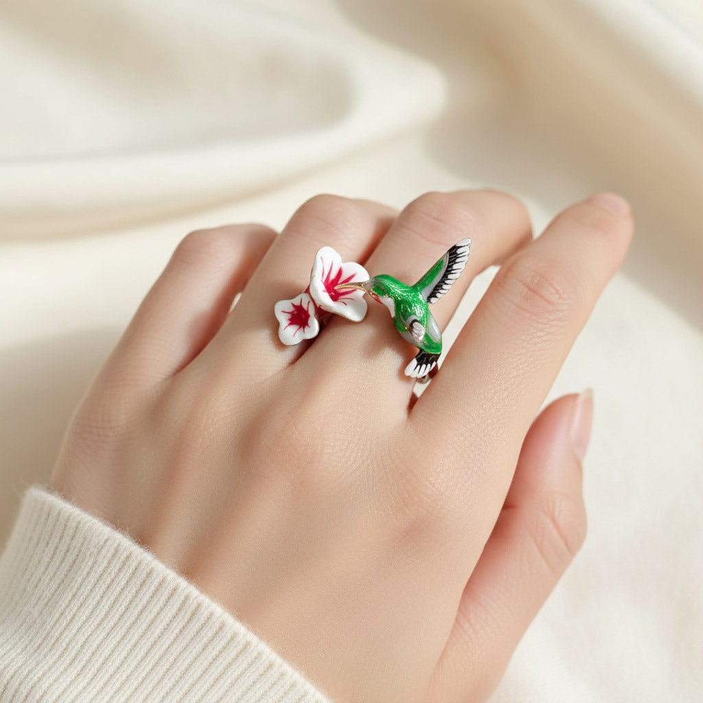 Hand wearing a ring with a green bird and red flower design on a beige background
