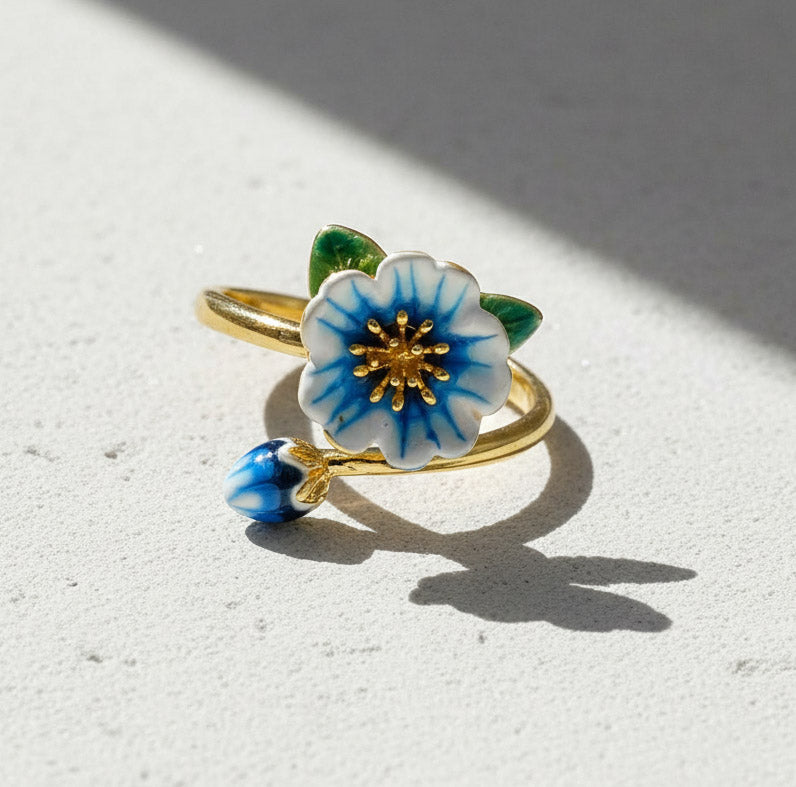 Gold ring with a blue and white floral design on a light surface