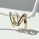 Gold linked ring set featuring green cubic zirconia stones, hanging on a white branch in sunlight.