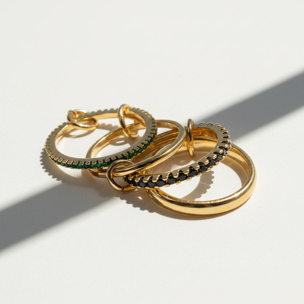 Stack of gold rings with green cubic zirconia stones on a light background