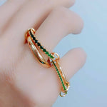 A set of four linked gold-plated rings with rich emerald cubic zirconia stones, worn across multiple fingers to showcase their adjustable design and playful elegance.