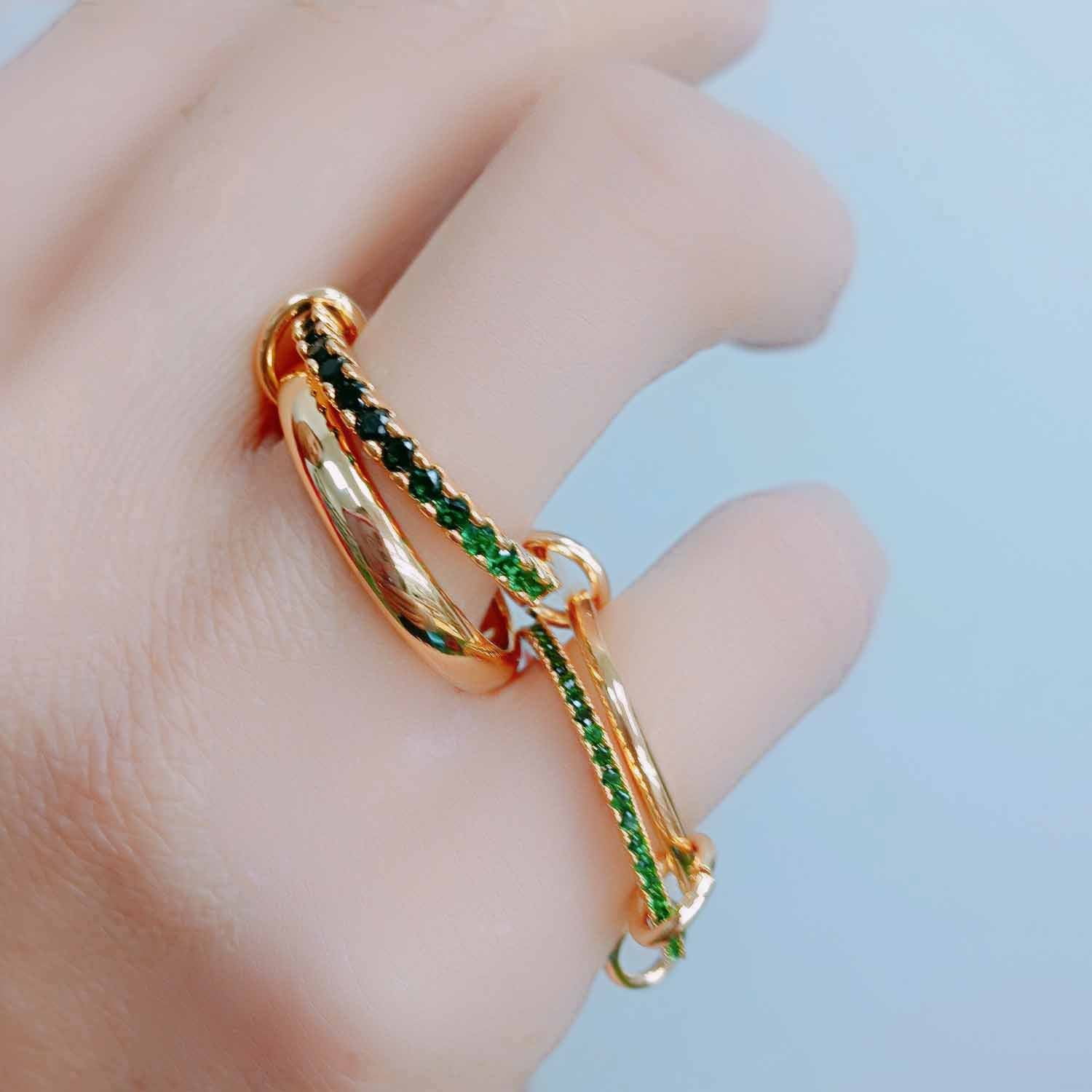 A set of four linked gold-plated rings with rich emerald cubic zirconia stones, worn across multiple fingers to showcase their adjustable design and playful elegance.