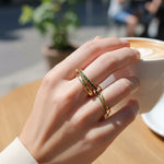 Hand wearing a gold ring with green gemstones in front of a cup of coffee.