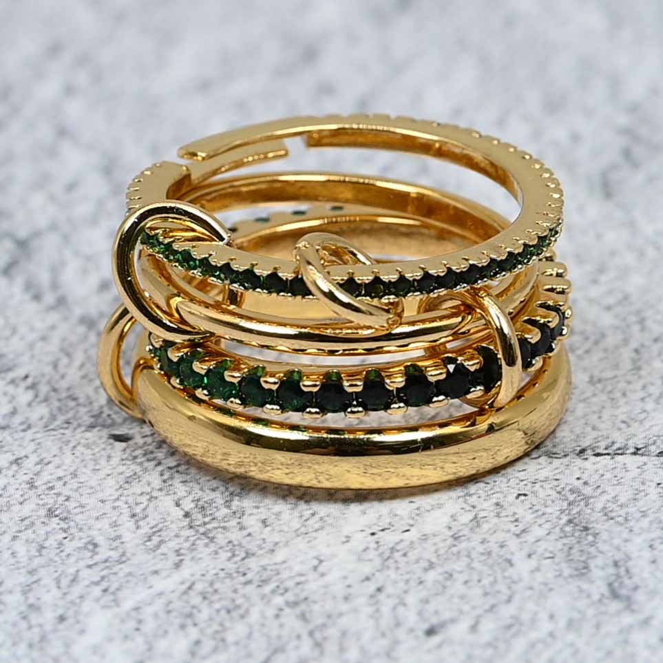 A close-up view of the four linked gold-plated rings with green cubic zirconia detailing, showcasing the polished and pavé finishes.