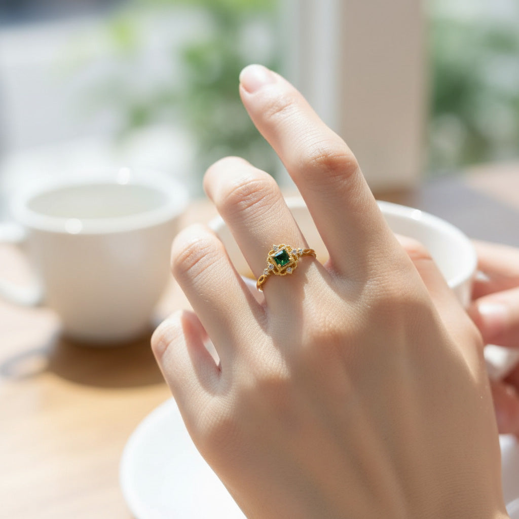 Hand wearing a gold ring with a green gemstone, blurred background